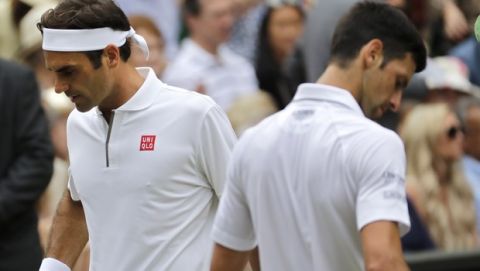 Switzerland's Roger Federer and Serbia's Novak Djokovic, right, pass each other when switching sides during the men's singles final match of the Wimbledon Tennis Championships in London, Sunday, July 14, 2019. (AP Photo/Ben Curtis)
