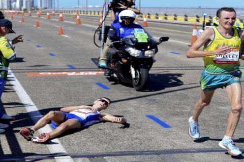 Australia's Michael Shelley, right, passes Callum Hawkins of Scotland after he collapsed during the men's marathon at the XXI Commonwealth Games on the Gold Coast, Australia, Sunday, April 15, 2018. Shelley won the marathon in dramatic fashion when leader Callum Hawkins of Scotland collapsed to the road with cramping with about two kilometers to go. Hawkins had about a two-minute lead over Shelley but became disoriented at about the 38-kilometer mark of the 42.2-kilometer-long race.(Tracey Nearmy/AAP Image via AP)