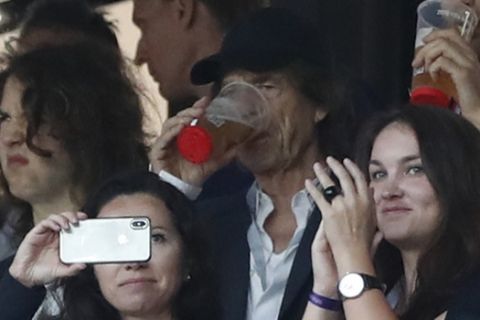 Singer Mick Jagger of the Rolling Stones, in black baseball hat, drinks a pint during the semifinal match between Croatia and England at the 2018 soccer World Cup in the Luzhniki Stadium in, Moscow, Russia, Wednesday, July 11, 2018. (AP Photo/Alastair Grant)