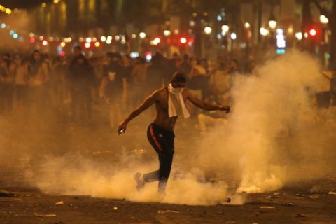 A man kicks a tear gas canister thrown by riot police during clashes on the Champs Champs Elysees avenue where soccer fans were celebrating France's World Cup victory over Croatia in Paris, France , Sunday, July 15, 2018 in Paris. France won its second World Cup title by beating Croatia 4-2. (AP Photo/Thibault Camus)