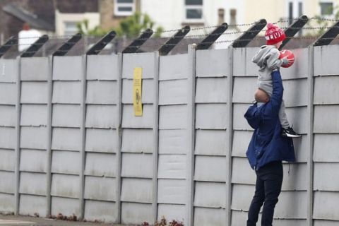 A man holds a child up over a fence to look into Liverpool's Melwood training ground after the English Premier League announced soccer players can return to training in small groups as the coronavirus lockdown was eased starting today Tuesday May 19, 2020. (Peter Byrne/PA via AP)