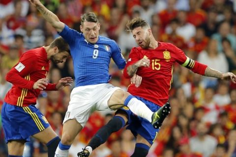 Italy's Andrea Belotti , center, jumps for the ball with Spain's Sergio Ramos, right, and Spain's Gerard Pique during the World Cup Group G qualifying soccer match between Spain and Italy at the Santiago Bernabeu Stadium in Madrid, Saturday Sept. 2, 2017. (AP Photo/Paul White)
