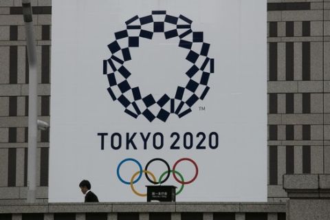 A man walks past a large banner promoting the Tokyo 2020 Olympics in Tokyo, Monday, March 23, 2020. The IOC will take up to four weeks to consider postponing the Tokyo Olympics amid mounting criticism of its handling of the coronavirus crisis that now includes Canada saying it won't send a team to the games this year and the leader of track and field, the biggest sport at the games, also calling for a delay. (AP Photo/Jae C. Hong)