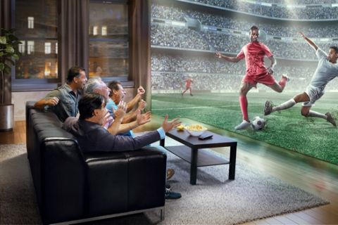 :biggrin:A group of four adult male friends are shocked while watching extremely realistic Soccer game on TV. They are sitting on a sofa in the modern living room faced to a real stadium with players instead of the front wall. It is evening outside the window.