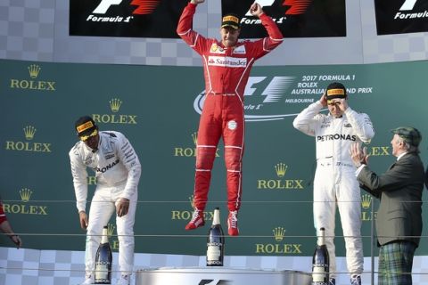 Ferrari driver Sebastian Vettel of Germany, center, jumps up as he arrives to the podium with Mercedes drivers Lewis Hamilton of Britain, left, and Valtteri Bottas of Finland as former world champion Jackie Stewart, right, applauds following the Australian Formula One Grand Prix in Melbourne, Australia, Sunday, March 26, 2017. Vettel won the race ahead of Hamilton and Bottas. (AP Photo/Rick Rycroft)