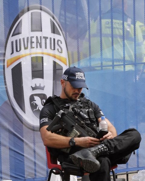 An armed police officer looks at his phone as he stands guard ahead of the Champions League final soccer match between Juventus and Real Madrid at the Millennium stadium in Cardiff, Wales Saturday June 3, 2017. (AP Photo/Frank Augstein)