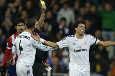 Real's Pepe, center, and Cristiano Ronaldo, right, laugh as Pepe gets a yellow card during the semifinal, 1st leg, Copa del Rey soccer derby match between Real Madrid and Atletico Madrid at the Santiago Bernabeu Stadium in Madrid, Wednesday Feb. 5, 2014. (AP Photo/Paul White)