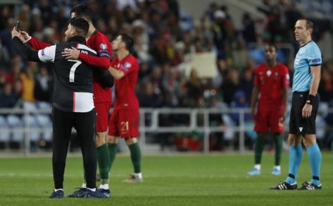 A supporter, who jumped into the pitch, takes a selfie with Portugal's Cristiano Ronaldo, second left, as French referee Ruddy Buquet looks at them during the Euro 2020 group B qualifying soccer match between Portugal and Lithuania at the Algarve stadium outside Faro, Portugal, Thursday, Nov. 14, 2019. (AP Photo/Armando Franca)