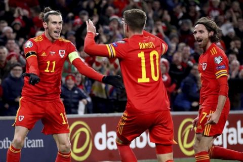 Wales' Aaron Ramsey celebrates scoring his side's first goal of the game against Hungary, with team-mates Gareth Bale, left, and Joe Allen, right, during  their UEFA Euro 2020 Qualifying soccer match at the Cardiff City Stadium, in Cardiff, Wales, Tuesday Nov. 19, 2019. (Nick Potts/PA via AP)