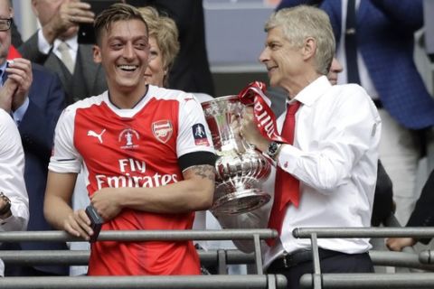 Arsenal team manager Arsene Wenger, right, holds the trophy next to Arsenal's Mesut Ozil after the English FA Cup final soccer match between Arsenal and Chelsea at the Wembley stadium in London, Saturday, May 27, 2017. (AP Photo/Matt Dunham)