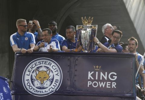 Leicester City's Kasper Schmeichel, left, chairman Vichai Srivaddhanaprabha, second from left, and Vice Chairman Aiyawatt Srivaddhanaprabha, right, with the trophy after winning the English Premier League during an open top bus parade through the central business district of Bangkok, Thailand, Thursday, May 19, 2016. The Leicester City team is on a two-day visit to Bangkok to celebrate their premiership win. Leicester City is owned by Thai duty free group King Power, run by Chairman and CEO Vichai Srivaddhanaprabha. (AP Photo/Sakchai Lalit)