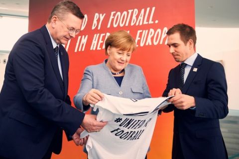 ARCHIVO - En esta fotografía de archivo del 26 de marzo de 2018, la canciller alemana Angela Merkel, al centro; el director de la Federación Alemana de Fútbol, Reinhard Grindel, izquierda, y el exjugador Philipp Lahm, derecha, promueven que Alemania sea sede de la Eurocopa de 2024, en Berlín. (Felix Zahn/dpa vía AP, archivo)