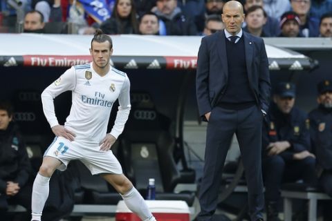 Real Madrid's Gareth Bale stretches next to Real Madrid's head coach Zinedine Zidane while waiting to come on as substitute during a Spanish La Liga soccer match between Real Madrid and Barcelona at the Santiago Bernabeu stadium in Madrid, Spain, Saturday, Dec. 23, 2017. (AP Photo/Paul White)