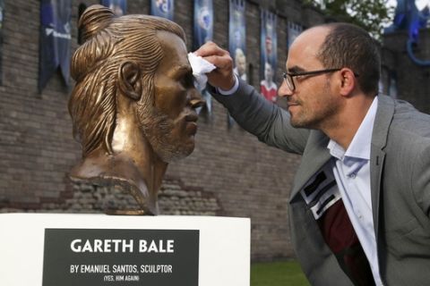 Artist Emanuel Santos, wipes a bust of Real Madrid and Wales soccer player Gareth Bale that he created, after it was placed on display in Cardiff, Wales Wednesday May 31, 2017, ahead of this weekend's Champions League final between Real Madrid and Juventus.  Santos is the artist behind the controversial recent Cristiano Ronaldo bust at Madeira airport. (Geoff Caddick/PA via AP)