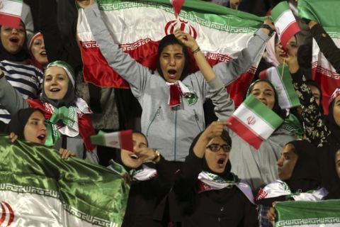 Female Iranian spectators cheer as they wave their country's flag during a friendly soccer match between Iran and Bolivia, at the Azadi (Freedom) stadium, in Tehran, Iran, Tuesday, Oct. 16, 2018. In a rare move, authorities allowed a select group of women into Azadi stadium to watch a men's soccer match. In Iran women are not allowed to watch men's soccer matches in stadiums, though they have occasionally been allowed to watch volleyball and basketball in stadiums. (AP Photo/Vahid Salemi)