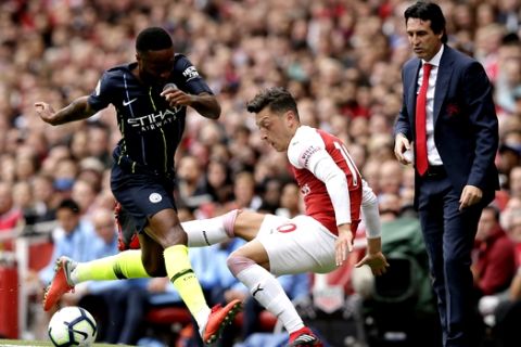 Arsenal manager Unai Emery, right, watches Manchester City's Raheem Sterling, left, fight for the ball with Arsenal's Mesut Ozil during the English Premier League soccer match between Arsenal and Manchester City at the Emirates stadium in London, England, Sunday, Aug. 12, 2018. (AP Photo/Tim Ireland)