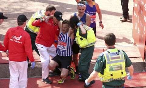 A runner is helped by medical staff after crossing the finish line during the 2018 Virgin Money London Marathon, Sunday April 22, 2018.  Medical condition of this competitor is unknown, but hot weather has proved to be a considerable problem for some runners. (Paul Harding/PA via AP)
