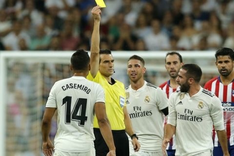 Real Madrid's Dani Carvajal, second right, is shown a yellow card by referee Juan Martinez Munuera after tackling Atletico Madrid's Koke, left on the ground, during a Spanish La Liga soccer match between Real Madrid and Atletico Madrid at the Santiago Bernabeu stadium in Madrid, Spain, Saturday, Sept. 29, 2018. (AP Photo/Paul White)