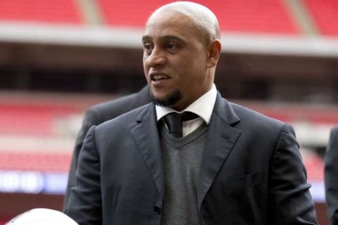 Former Brazil national soccer team player Roberto Carlos holds a ball as he attends a group photo session pitchside as a guest of FIFA Presidential Candidate Gianni Infantino after unveiling his 90 day plan that he will implement if he is elected FIFA President, at Wembley Stadium in London, Monday, Feb. 1, 2016. (AP Photo/Matt Dunham)