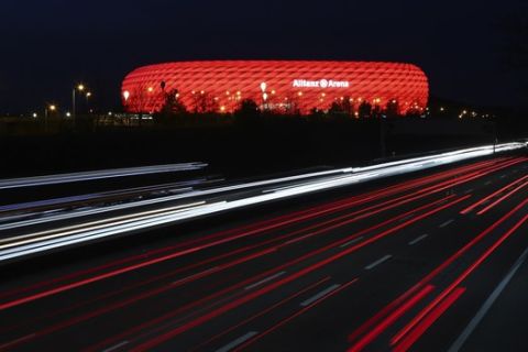 Cars pass the illuminated 'Allianz Arena' soccer stadium in Munich, Germany, Monday, March 16, 2020. UEFA, are set to make a final decision when the UEFA executive committee meets on Tuesday March 17, 2020 after talks with clubs and leagues, about possibly delaying the Euro 2020 soccer tournament by a year as the continent grapples with the outbreak of the coronavirus. (AP Photo/Matthias Schrader)