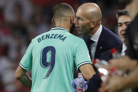 Real Madrid's head coach Zinedine Zidane, right, talks to Real Madrid's Karim Benzema after he scoried his side's opening goal during the Spanish La Liga soccer match between Sevilla and Real Madrid at the Ramon Sanchez Pizjuan stadium in Seville, Spain, Sunday, Sept. 22, 2019. (AP Photo/Miguel Morenatti)