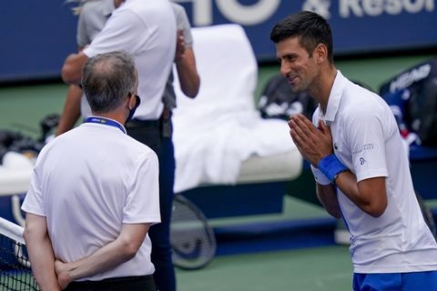 Novak Djokovic, of Serbia, talks with the umpire after inadvertently hitting a line judge with a ball after hitting it in reaction to losing a point against Pablo Carreno Busta, of Spain, during the fourth round of the US Open tennis championships, Sunday, Sept. 6, 2020, in New York. Djokovic defaulted the match. (AP Photo/Seth Wenig)
