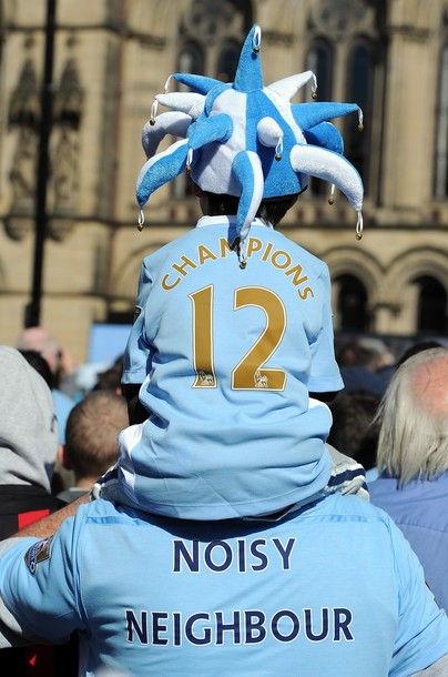 MANCHESTER, ENGLAND - MAY 14: Manchester City fans wear shirts displaying the messages "Champions" and "Noisy Neighbour" as they look on in front of Manchester Town Hall before the start of the victory parade around the streets of Manchester on May 14, 2012 in Manchester, United Kingdom.  (Photo by Chris Brunskill/Getty Images)