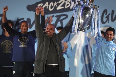 Manchester City coach Pep Guardiola, left, and his assistant Mikel Arteta hold the trophy as they celebrate with their supporters at the Etihad Stadium in Manchester, England, Sunday May 12, 2019 the day they won the English Premier League title. Manchester City retained the Premier League trophy after coming from behind to beat Brighton 4-1 and see off Liverpool's relentless challenge on the final day of the season on Sunday. (AP Photo/Jon Super)