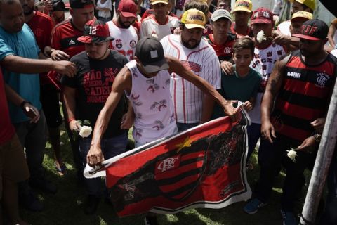 A fan holds a Flamengo flag as he and other fans pay a homage to the fire victims at the entrance Flamengo soccer club training complex in Rio de Janeiro, Brazil, Friday, Feb. 8, 2019. A fire tore through the sleeping quarters of the Flamengo soccer club development league, one of Brazil's most popular professional soccer clubs, killing several people who were most likely players and injuring others, authorities said. (AP Photo/Leo Correa)