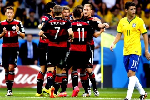 Brazil's Oscar, right, passes by celebrating German players after Germany's Thomas Mueller scored the opening goal during the World Cup semifinal soccer match between Brazil and Germany at the Mineirao Stadium in Belo Horizonte, Brazil, Tuesday, July 8, 2014. (AP Photo/Frank Augstein)