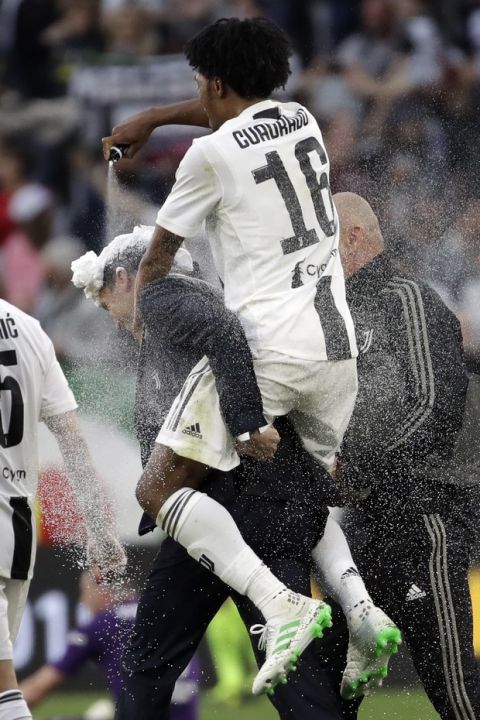 Juventus' Juan Cuadrado, right, sprays foam over Juventus coach Massimiliano Allegri at the end of a Serie A soccer match between Juventus and AC Fiorentina, at the Allianz stadium in Turin, Italy, Saturday, April 20, 2019. Juventus clinched a record-extending eighth successive Serie A title, with five matches to spare, after it defeated Fiorentina 2-1. (AP Photo/Luca Bruno)