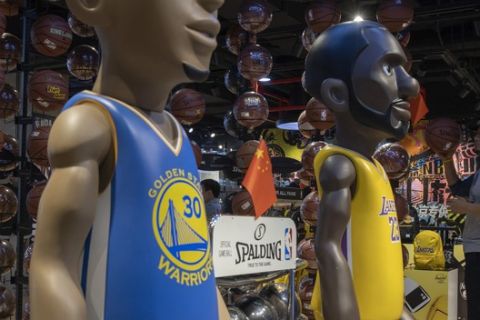 In this Friday, Oct. 11, 2019, photo, a shopper reach holds a basketball near statues of NBA players Stephen Curry of the Golden State Warriors, left, and Lebron James of the Los Angeles Lakers holding Chinese flags in the entrance of an NBA merchandise store Beijing. When Houston Rockets' general manager Daryl Morey tweeted last week in support of anti-government protests in Hong Kong, everything changed for NBA fans in China. A new chant flooded Chinese sports forums: "I can live without basketball, but I can't live without my motherland." (AP Photo/Ng Han Guan)