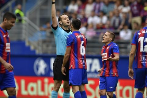 The referee shows a yellow card to Eibar's Sergio Alvarez after a tackle on Barcelona's Lionel Messi during a Spanish La Liga soccer match between Eibar and FC Barcelona at the Ipurua stadium in Eibar, Spain, Saturday Oct. 19, 2019. (AP Photo/Alvaro Barrientos)