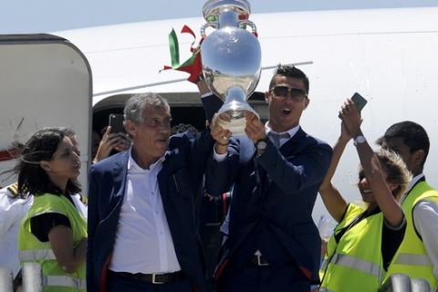 Portugal's Cristiano Ronaldo and coach Fernando Santos, left, lift the Euro 2016 trophy after defeating France in the final, as they arrive at the Humberto Delgado Airport in Lisbon, Portugal, Monday, July 11, 2016. (AP Photo/Paulo Duarte)