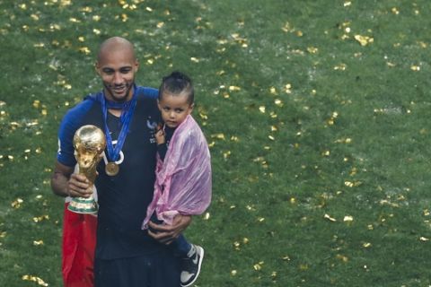 France's Steven Nzonzi poses for photos holding the trophy and a child at the end of the final match between France and Croatia at the 2018 soccer World Cup in the Luzhniki Stadium in Moscow, Russia, Sunday, July 15, 2018. (AP Photo/Rebecca Blackwell)