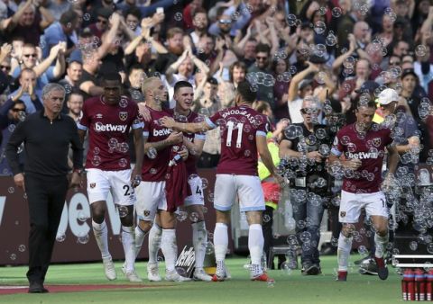 Manchester United manager Jose Mourinho, left, walks past West Ham's Marko Arnautovic, 3rd left, who celebrates with teammates after scoring his sides third goal during the English Premier League soccer match between West Ham United and Manchester United at London Stadium in London in London, England, Saturday, Sept. 29, 2018. (AP Photo/Tim Ireland)