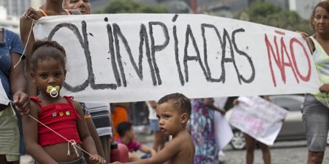 Children stand next to a banner that reads in Portuguese "Olympics no" during a protest against the housing shortage and the money spent on the upcoming Olympics Games in Rio de Janeiro, Brazil, Tuesday, March 31, 2015. The demonstrators were evicted recently from a parking lot at the state water and sewage company, CEDAE, where they were living for one week. (AP Photo/Silvia Izquierdo)