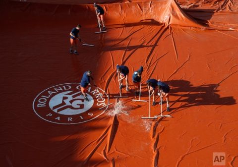In this Tuesday, June 6, 2017 photo, workers remove water from the tarpaulin covering the court as rain showers suspended the quarterfinal match of Denmark's Caroline Wozniacki and Latvia's Jelena Ostapenko of the French Open tennis tournament at the Roland Garros stadium, in Paris, France. (AP Photo/Petr David Josek)