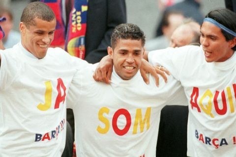 Barcelona's Brazilian players Rivaldo, left, Sonny Anderson, center, and Giovanni celebrate on an open double decker bus that paraded through Barcelona, Spain Monday May 24, 1999. Barcelona were proclaimed Spanish league champions last Saturday after beating Alaves. Their  T-Shirts, written in Catalan,  read " We are here" in reference to arriving in Barcelona's Plaza Saint Jaume, where they always celebrate title wins. (AP Photo/Paul White)