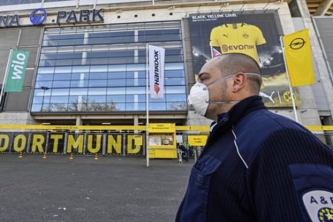 Security with face masks stand in front of the Signal Iduna Park, Germany's biggest stadium of Bundesliga soccer club Borussia Dortmund, where a temporary coronavirus treatment center opened today in Dortmund, Germany, Saturday, April 4, 2020. Instead of the originally scheduled today football clash between Dortmund and Bayern, parts of the stadium were turned into a medical center for outpatient treatment and consultation. The new coronavirus causes mild or moderate symptoms for most people, but for some, especially older adults and people with existing health problems, it can cause more severe illness or death. (AP Photo/Martin Meissner)