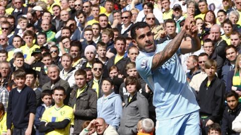 Manchester City's Carlos Tevez celebrates with a golf swing after scoring the fifth goal of the game his hat trick in front of dejected Norwich City fans