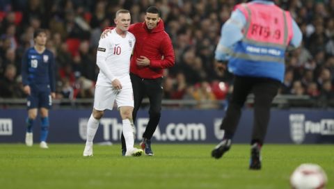 A pitch invader goes up to England's Wayne Rooney as a guard runs up to catch him during the international friendly soccer match between England and the United States at Wembley stadium, Thursday, Nov. 15, 2018. (AP Photo/Alastair Grant)