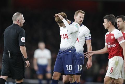 Tottenham's Dele Alli, center touches his head after a bottle was thrown at him from the stands during the English League Cup quarter final soccer match between Arsenal and Tottenham Hotspur at the Emirates stadium in London, Wednesday, Dec. 19, 2018. (AP Photo/Frank Augstein)