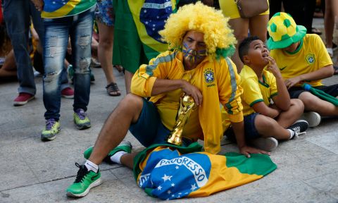 Brazil soccer fans sit dejectedly on the ground as they watch a live telecast of the Brazil vs. Belgium World Cup quarter finals soccer match, in Rio de Janeiro, Brazil, Friday, July 6, 2018. (AP Photo/Silvia Izquierdo)