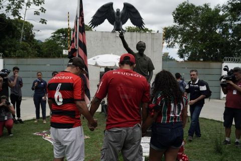Fans hold hands as they pray in a homage to the victims of a fire at the Flamengo soccer club training complex in Rio de Janeiro, Brazil, Friday, Feb. 8, 2019. A fire tore through the sleeping quarters of the Flamengo soccer club development league, one of Brazil's most popular professional soccer clubs, killing several people who were most likely players and injuring others, authorities said. (AP Photo/Leo Correa)