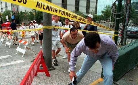Spectators duck under security lines to cross Williams Street in downtown Atlanta Sunday, July 28, 1996. One woman was killed and more than 100 people were wounded early Saturday when a pipe bomb detonated in the Centennial Olympic Park during a  concert. (AP Photo/Thomas Kienzle)