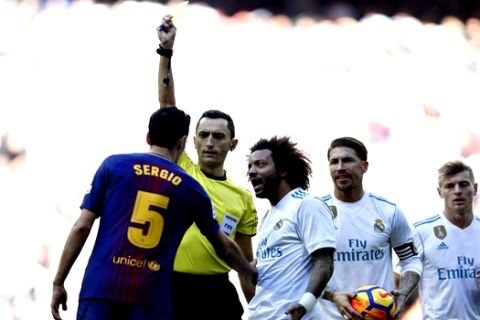Real Madrid's Marcelo , center, gestures while Referee Jose Maria Sanchez Martinez shows a yellow card to Barcelona's Sergio Busquets, left, during the Spanish La Liga soccer match between Real Madrid and Barcelona at the Santiago Bernabeu stadium in Madrid, Spain, Saturday, Dec. 23, 2017. (AP Photo/Francisco Seco)