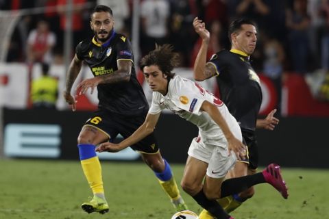 Sevilla's Bryan Gil, center, is tackled by APOEL's Lucas Souza during the Europa League group A soccer match between Sevilla and APOEL Nicosia at the Estadio Ramon Sanchez-Pizjuan stadium in Seville, Spain, Thursday, Oct. 3, 2019. (AP Photo/Miguel Morenatti)