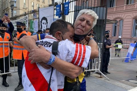 Soccer fans of rival soccer teams Boca Juniors, right, and River Plate, left, embrace as they wait to enter the presidential palace to see Diego Maradona lying in state in Buenos Aires, Argentina, Thursday, Nov. 26, 2020. The Argentine soccer great who led his country to the 1986 World Cup title died Wednesday at the age of 60. (AP Photo/Debora Rey)