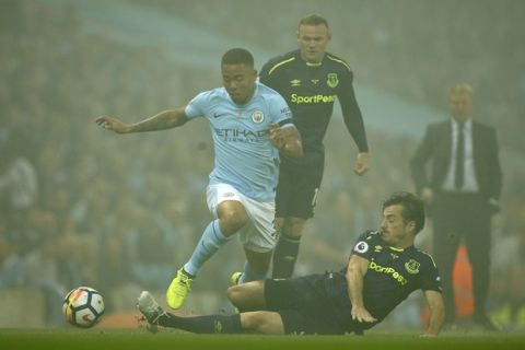 Shrouded in smoke from fireworks, Everton's Leighton Baines tackles Manchester City's Gabriel Jesus, with Wayne Rooney behind, during the English Premier League soccer match between Manchester City and Everton at the Etihad Stadium in Manchester, England, Monday, Aug. 21, 2017. (AP Photo/Dave Thompson)